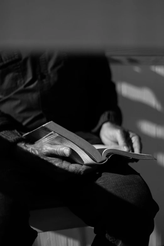 a man sitting on a bench reading a book, a black and white photo, by Jan Rustem, worship, hands, holding books, 6 : 3 0 am