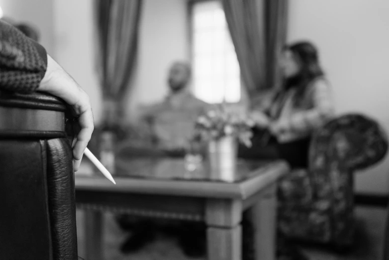 a person sitting on a couch with a cigarette in their hand, a black and white photo, by Kristian Zahrtmann, pexels contest winner, sitting at the parlament meeting, back of hand on the table, man holding spear, smoking woman