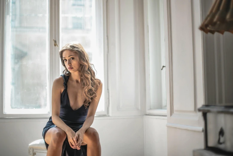 a woman sitting on a stool in front of a window, a portrait, by Emma Andijewska, pexels contest winner, wearing a low cut tanktop, wearing a cocktail dress, sofya emelenko, gorgeous stella maeve magician