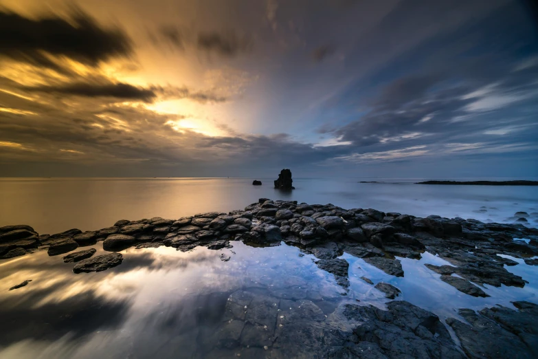 a body of water surrounded by rocks under a cloudy sky, sunset with cloudy skies, hd award-winning photo, image full of reflections, youtube thumbnail