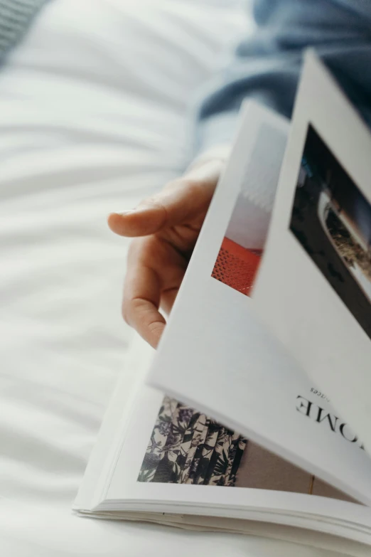 a person holding a book on top of a bed, magazine photograph, zoomed in, ignant, on white paper