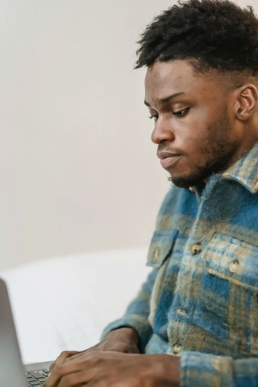 a man sitting in front of a laptop computer, by Carey Morris, trending on pexels, wearing blue jacket, man is with black skin, overcast, studious