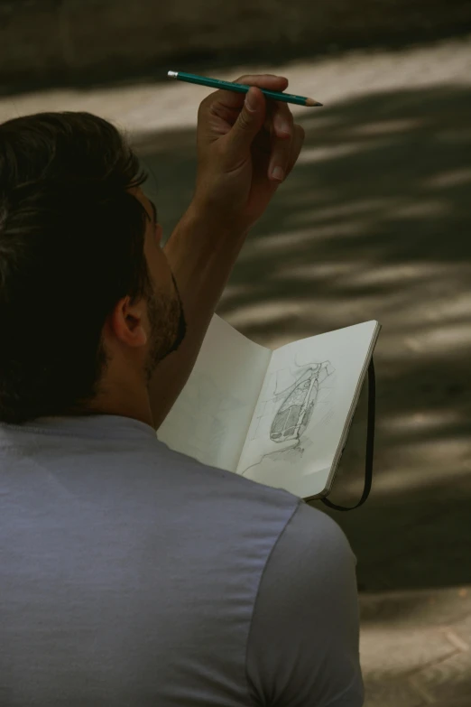 a man that is sitting down with a pen in his hand, a drawing, pexels contest winner, plein air, sketch book, perfectly shaded body, ignant, pictured from the shoulders up