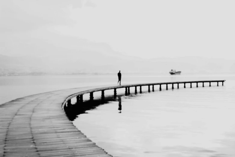 a black and white photo of a person standing on a dock, a black and white photo, by Niyazi Selimoglu, saatchi art, alone!!, peaceful day, hes alone