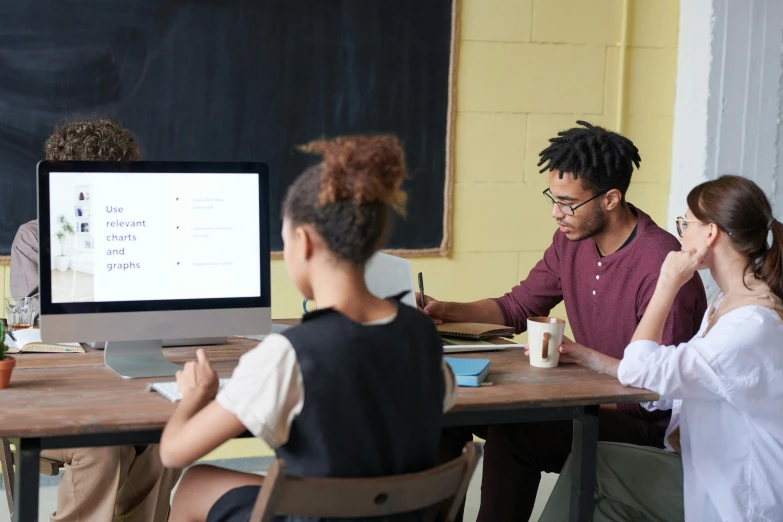 a group of people sitting around a wooden table, trending on pexels, academic art, large computer monitor, teacher, product introduction photo