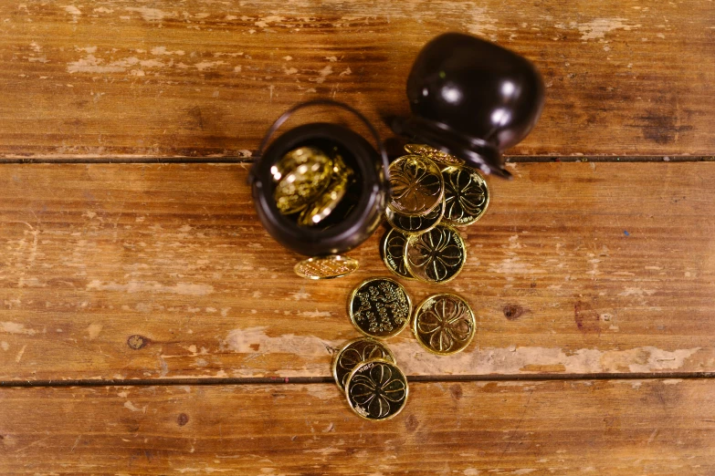 a pair of earrings sitting on top of a wooden table, scattered gold coins, 4 cannabis pots, black resin, thumbnail