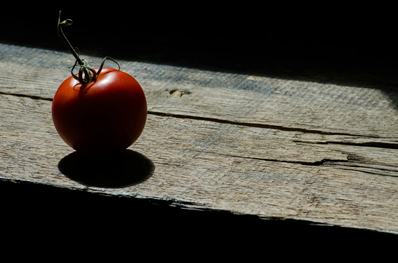 a tomato sitting on top of a wooden table, by Niko Henrichon, unsplash, in the shadows, ignant, tourist photo, uncrop