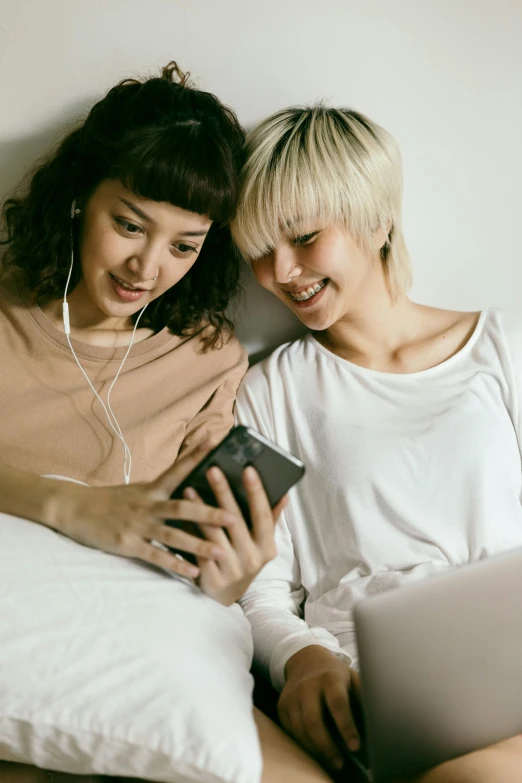 a couple of women sitting next to each other on a bed, by Jang Seung-eop, trending on pexels, happening, with head phones, one blonde and one brunette, mobile app, everything fits on the screen