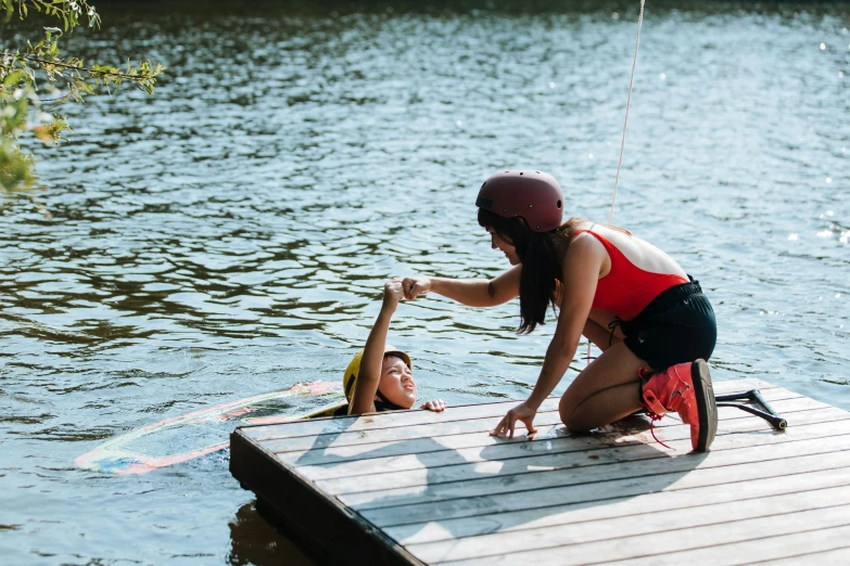 a woman standing on top of a wooden dock next to a man on a surfboard, reaching out to each other, belaying, mini lake, gofl course and swimming