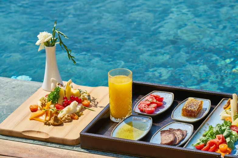 a tray of food sitting on top of a table next to a pool, by Julia Pishtar, gourmet restaurant, turquoise water, hearty breakfast, glazed