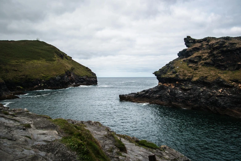 a man standing on top of a cliff next to a body of water, merlin, slate, large head, /r/earthporn