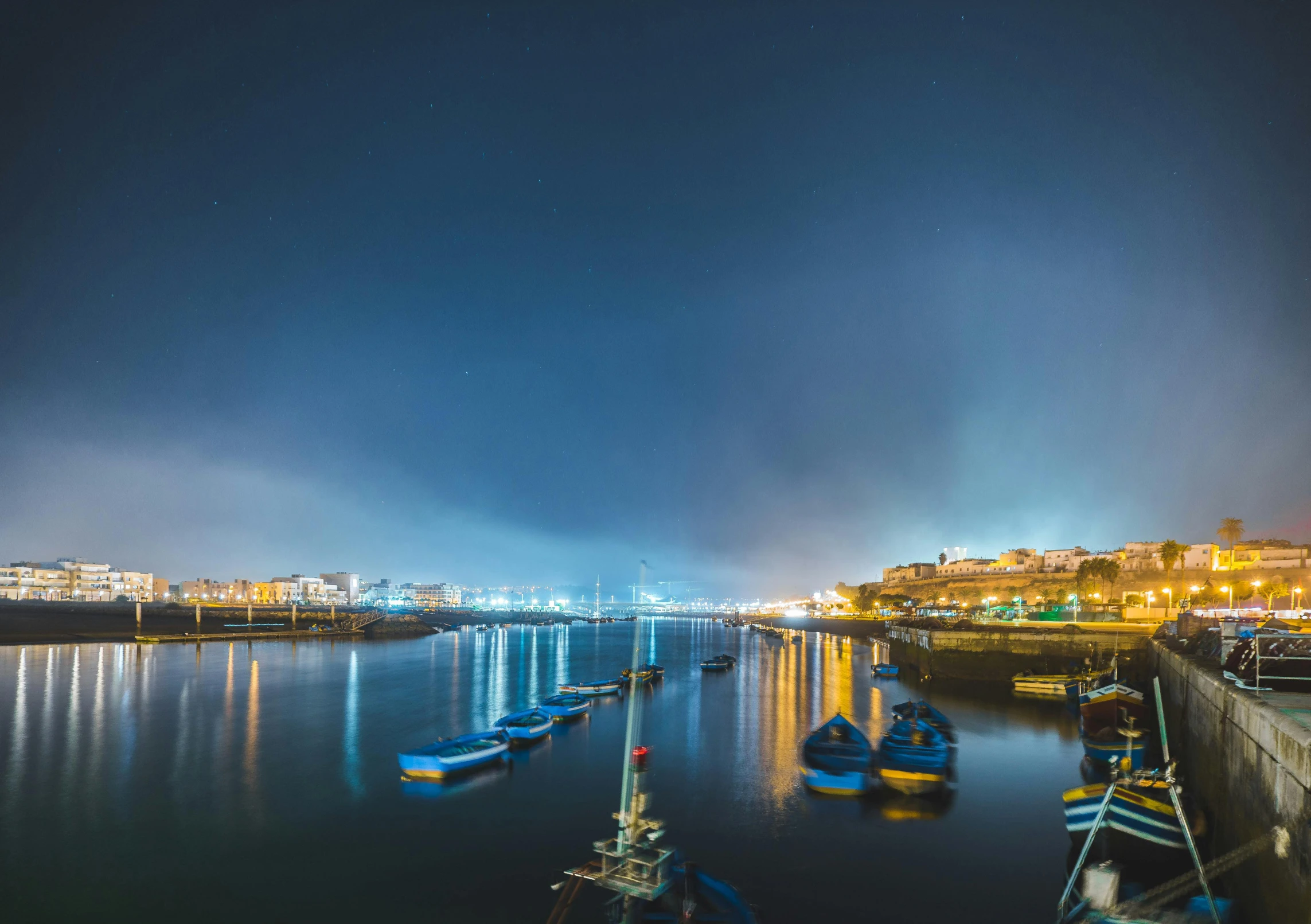 a group of boats floating on top of a body of water, by Matthias Stom, pexels contest winner, lisbon city at night, maryport, vibrant but dreary blue, panorama