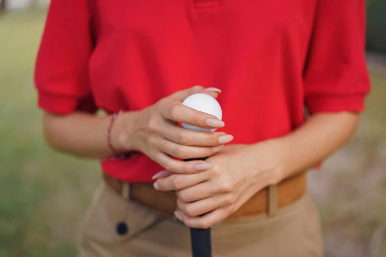 a woman in a red shirt holding a golf club, trending on unsplash, wearing a white button up shirt, partially cupping her hands, corrected hands, holding a ball