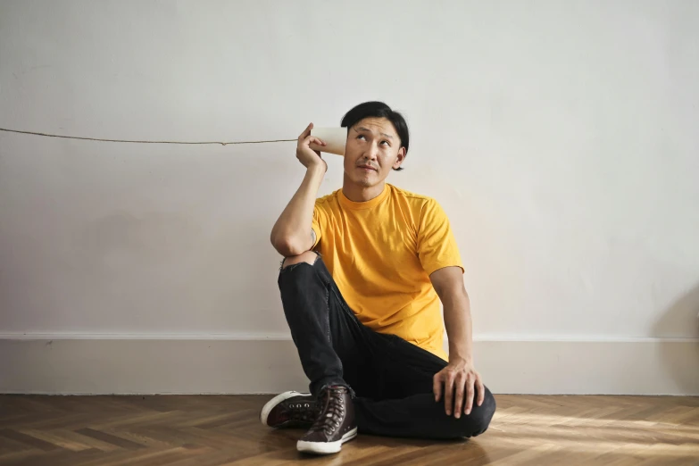 a man sitting on the floor listening to headphones, inspired by Fei Danxu, pexels contest winner, hyperrealism, wearing a modern yellow tshirt, holding a wooden staff, golden thread, asian descent