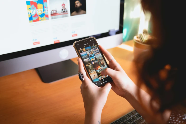 a woman holding a smart phone in front of a computer, a picture, trending on pexels, 🦩🪐🐞👩🏻🦳, photo for magazine, playing games, 9 9 designs