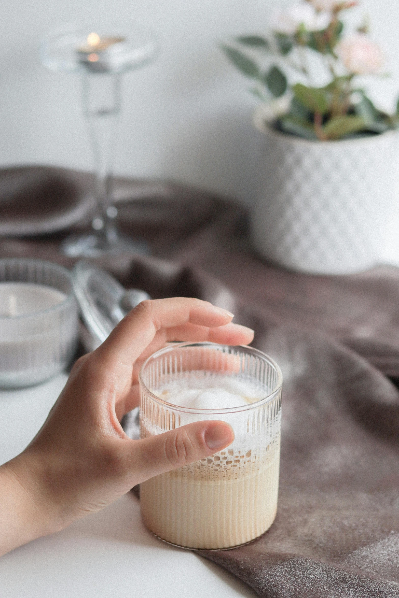 a person holding a cup of coffee on a table, vanilla smoothie explosion, at home, glassware, subtle detailing