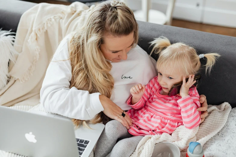 a woman sitting on a couch with a little girl, pexels contest winner, programming, blonde, brand, nursing