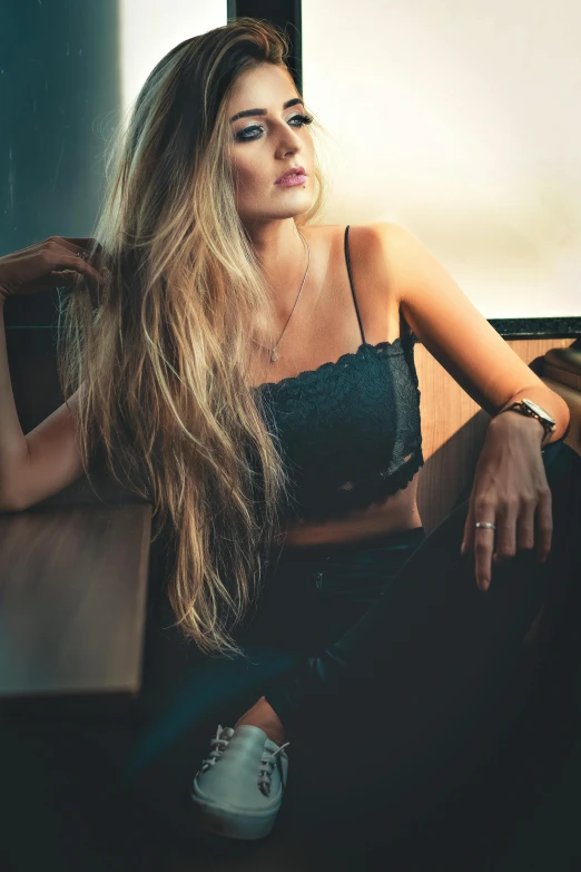 a woman sitting at a table in front of a window, a colorized photo, inspired by Elsa Bleda, trending on pexels, sexy girl with long blonde hair, wearing a cropped black tank top, long mane, confident relaxed pose