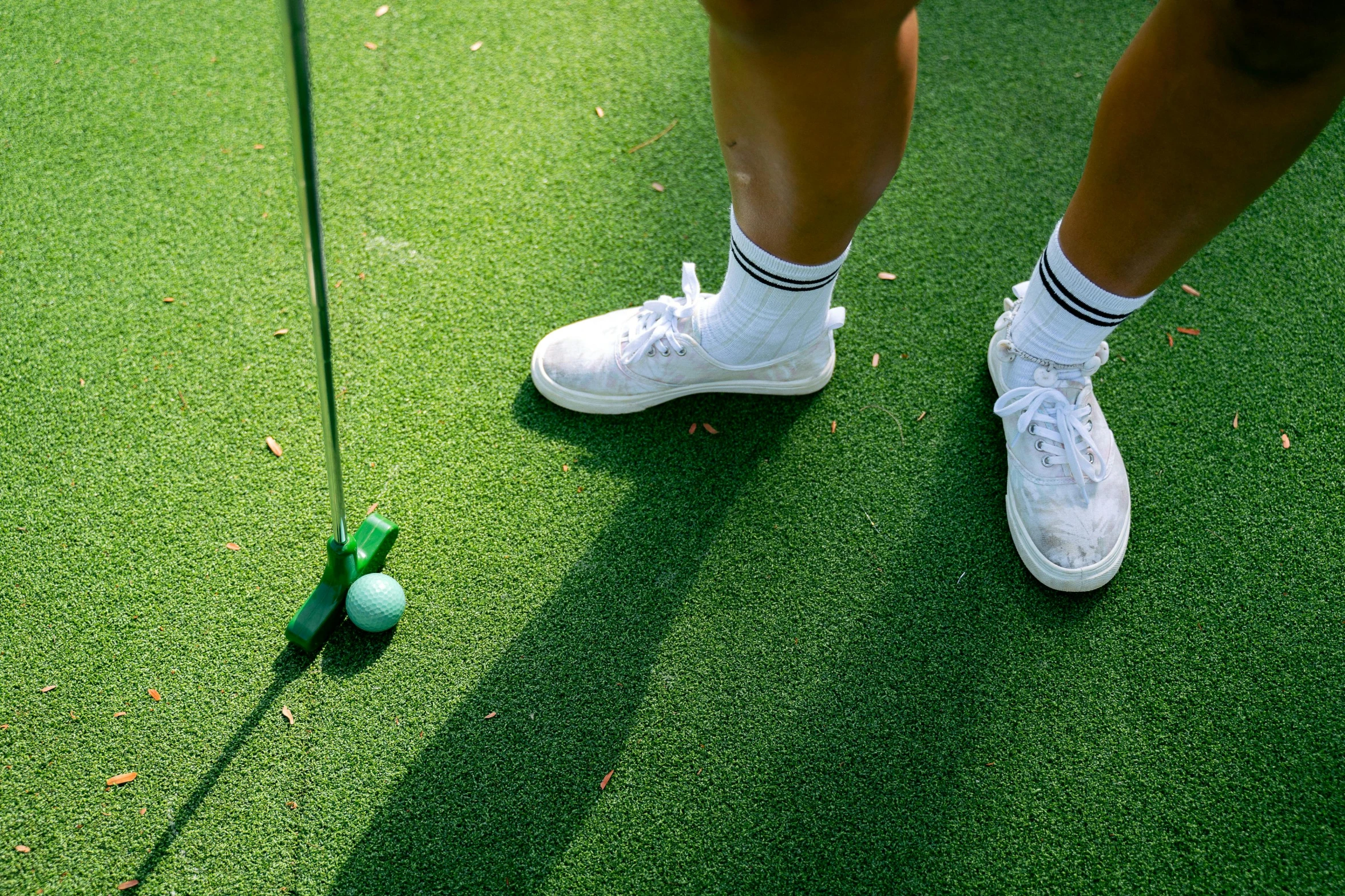 a woman standing on top of a green field next to a golf ball, leg and thigh shot, off putting, fake grass, top down shot