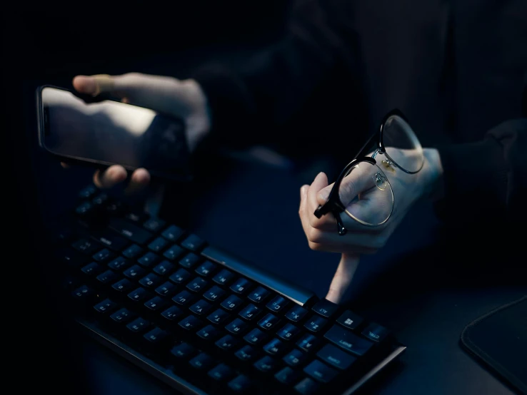 a close up of a person holding a cell phone near a keyboard, a computer rendering, unsplash, serial art, man steal computers, wearing black rimmed glasses, skin on the gaming pc, avatar image