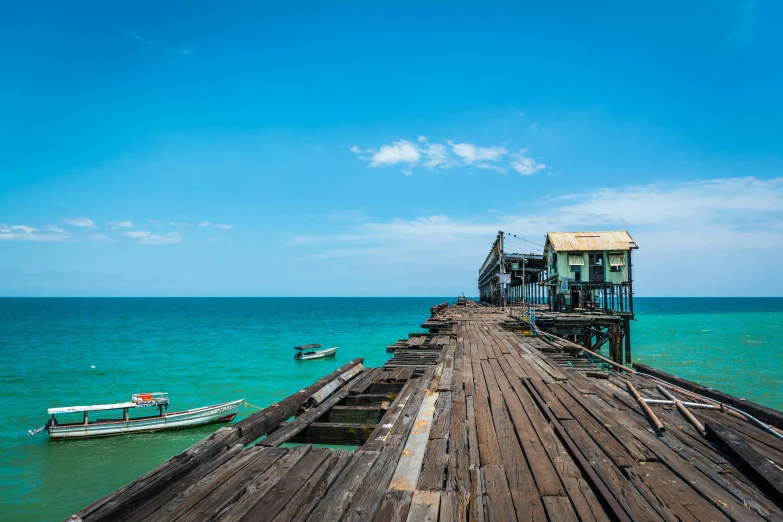 a boat sitting on top of a wooden pier, by Peter Churcher, pexels contest winner, sumatraism, yellow and cyan color palette, houses on stilts, view of the ocean, smoldering