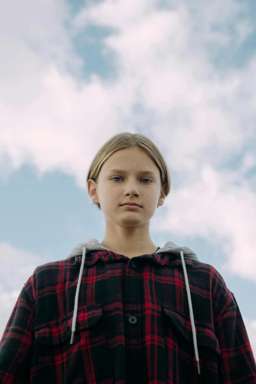 a young man standing in front of a cloudy sky, an album cover, unsplash, hyperrealism, greta thunberg, tartan hoodie, still from a music video, little girl