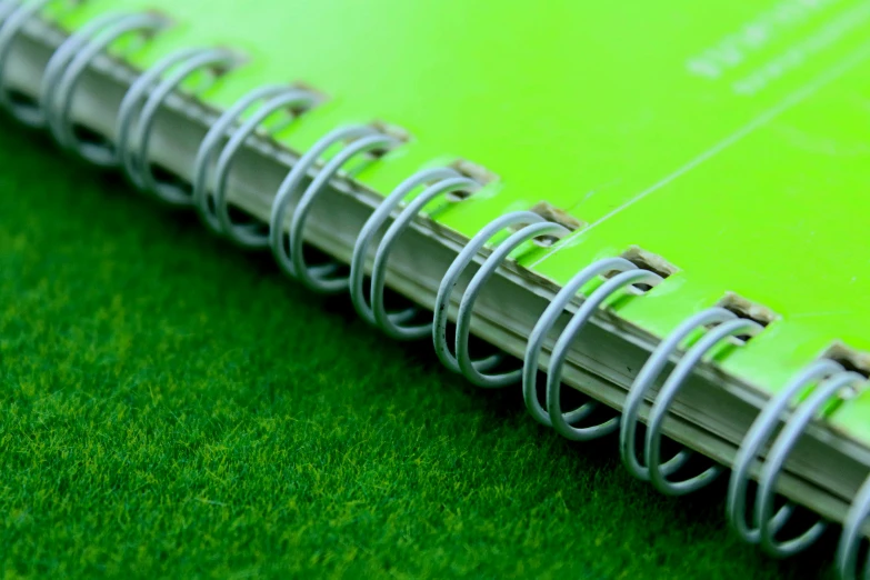 a green notebook sitting on top of a lush green field, a macro photograph, pexels, private press, neon green, turf roof, maths, close up shot from the side