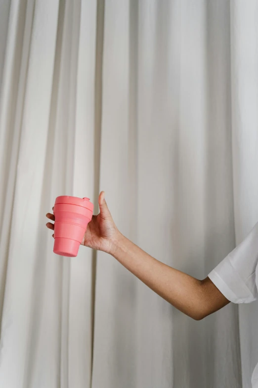 a woman holding a pink cup in front of a curtain, sustainable materials, silicone skin, detailed product image, folded