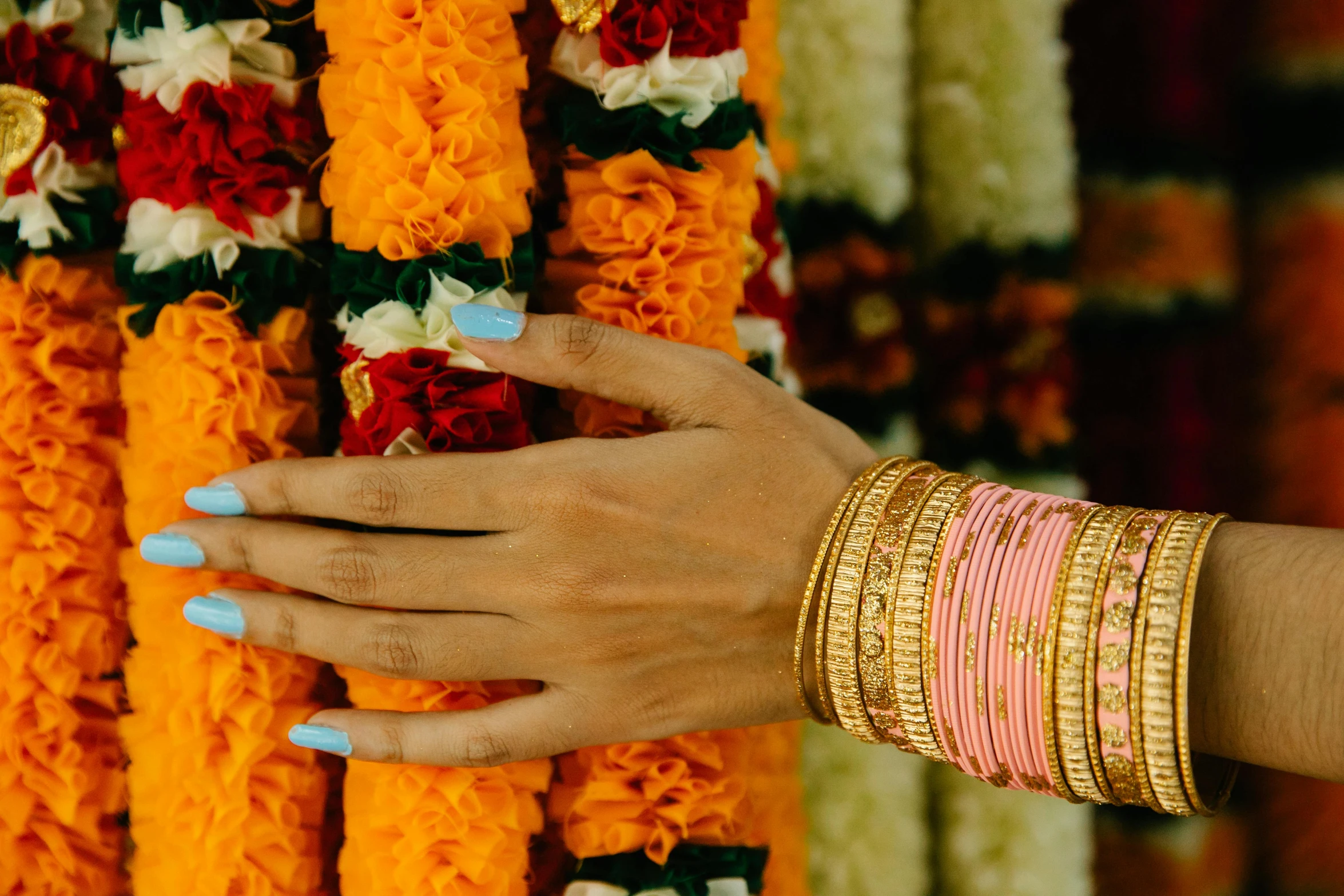 a close up of a person's hand near a bunch of flowers, by Alice Mason, hurufiyya, bangles, inside her temple, pink and orange, gold layers