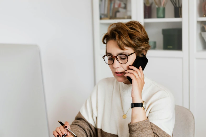a woman sitting at a desk talking on a cell phone, trending on pexels, brown and white color scheme, wearing medium - sized glasses, thumbnail, abcdefghijklmnopqrstuvwxyz