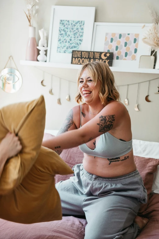 a woman sitting on top of a bed next to a pillow, a tattoo, pregnant belly, laughing maniacally, supportive, indi creates