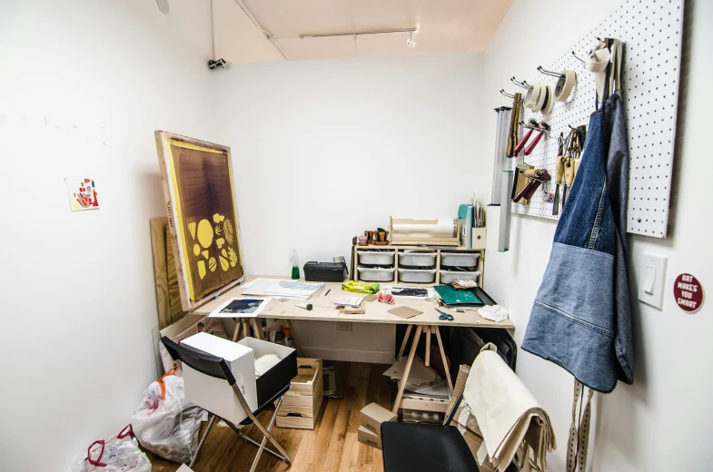 a room with a desk, chair, and pictures on the wall, a silk screen, unsplash, process art, workbench, resin and clay art, intrincate clothing, in oil”