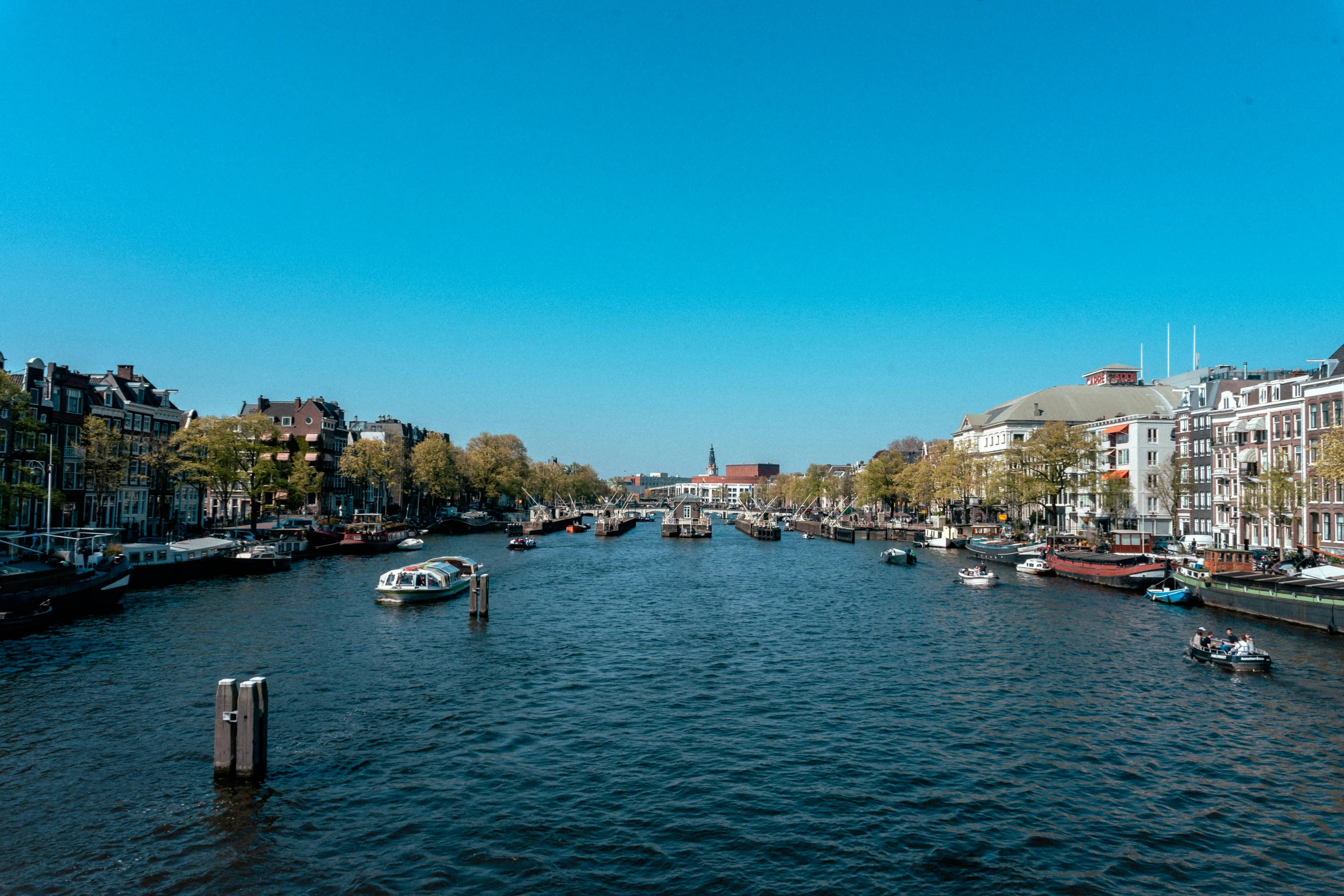 a river filled with lots of boats next to tall buildings, a photo, by Jan Tengnagel, clear blue skies, jan vermeer, thumbnail, high resolution image