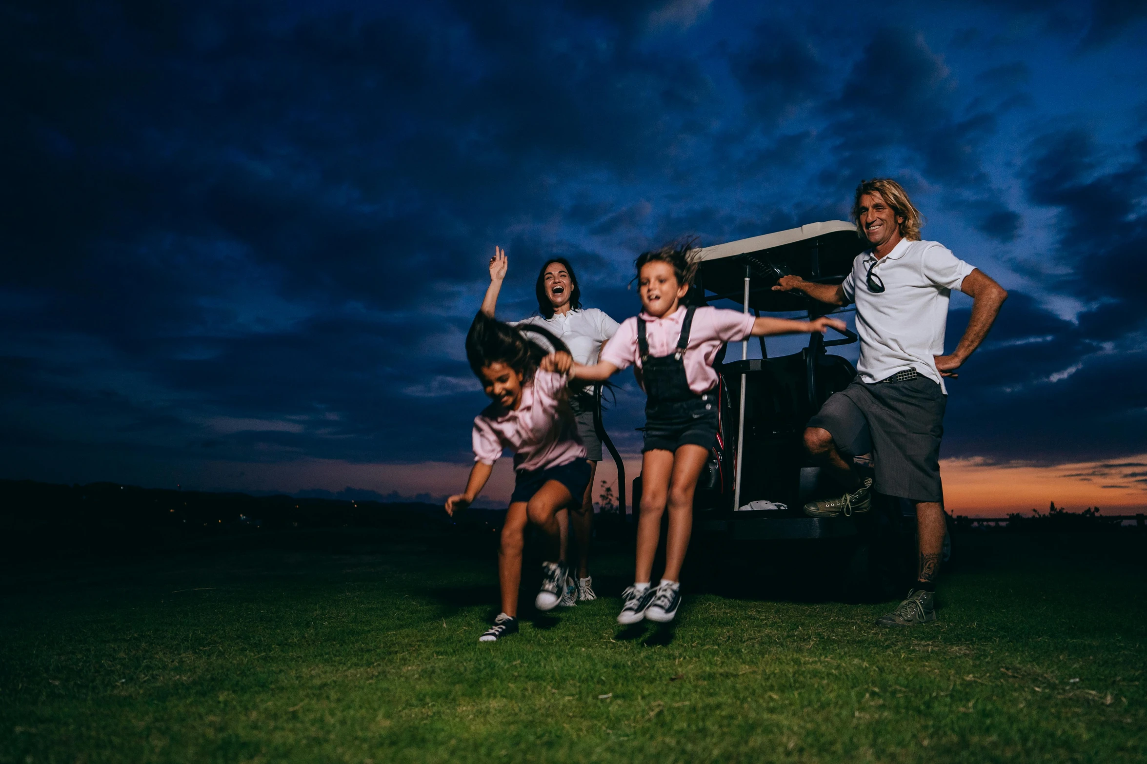 a group of people standing on top of a lush green field, during the night, kombi, playful pose, wearing golf shorts