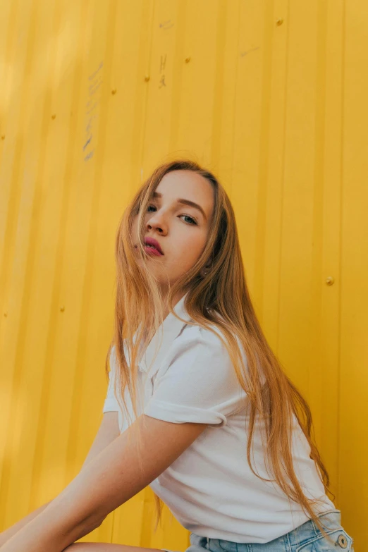 a woman sitting on the ground in front of a yellow wall, inspired by Elsa Bleda, trending on pexels, realism, long golden hair, portrait of white teenage girl, 15081959 21121991 01012000 4k, headshot profile picture