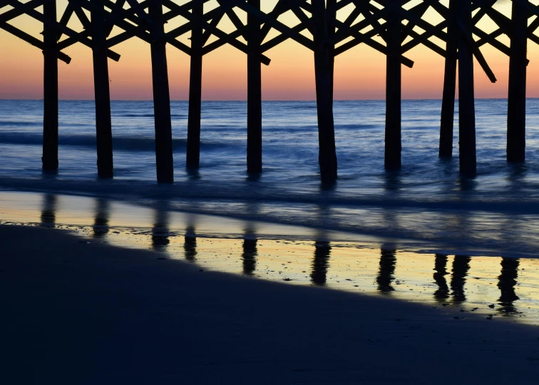 a group of people standing on top of a beach next to a pier, by Dave Melvin, art photography, reflection on the oil, predawn, close-up photograph, a wooden