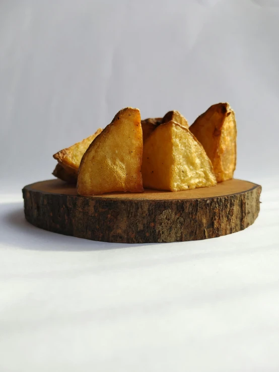 a pile of potatoes sitting on top of a wooden cutting board, by Jessie Algie, new sculpture, golden pyramids, pastries, profile pic, crispy quality