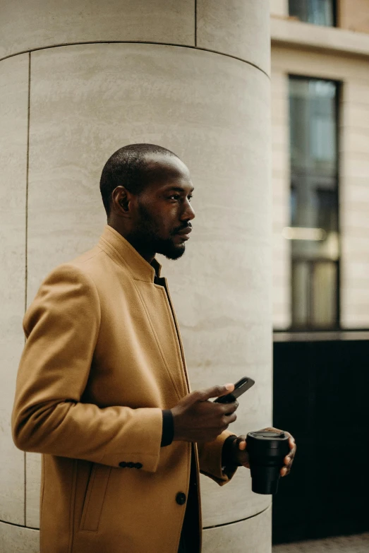 a man in a tan coat looking at his cell phone, pexels contest winner, virgil abloh, gold suit, short brown beard, walking confidently