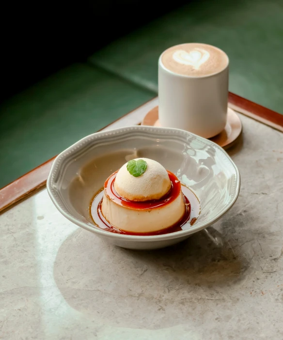 a white plate topped with a dessert next to a cup of coffee, inspired by Richmond Barthé, renaissance, bao phan, thumbnail, molten, bowl