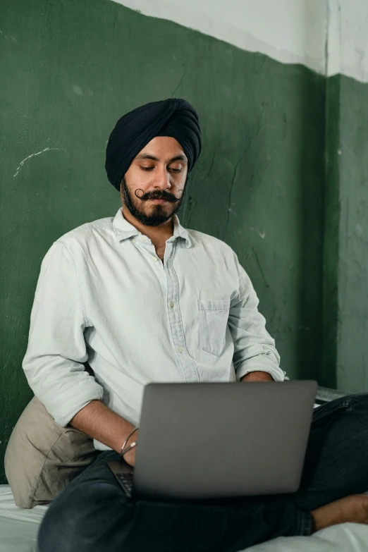 a man sitting on a bed using a laptop, inspired by Manjit Bawa, trending on pexels, in a school classroom, turban, mexican mustache, avatar image