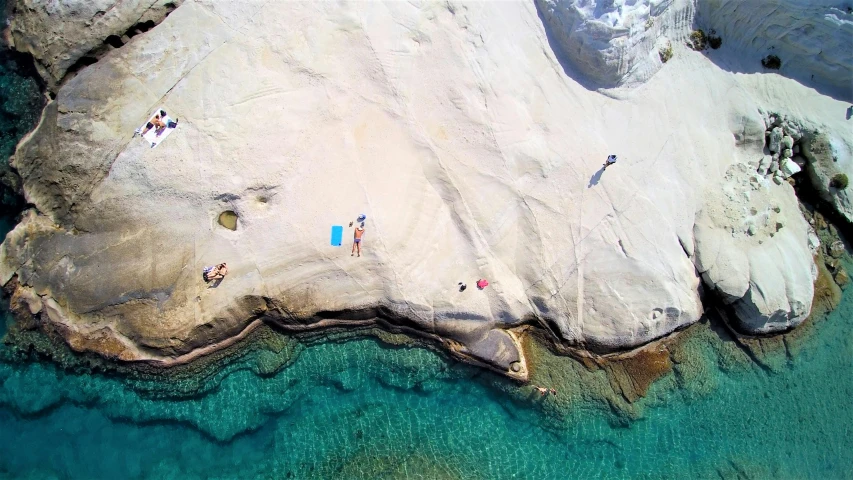 a group of people laying on top of a rock next to the ocean, by Alexis Grimou, pexels contest winner, aerial iridecent veins, greek nose, white sand, video still