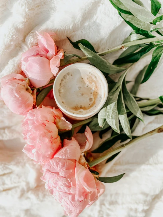 a cup of coffee sitting on top of a white blanket, by Lucia Peka, trending on unsplash, romanticism, pink flowers, low quality photo, 🎀 🧟 🍓 🧚, iced latte