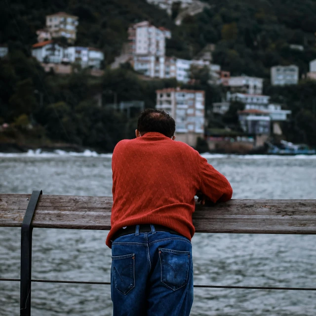 a man looking out over a body of water, by Tamas Galambos, pexels contest winner, realism, red sweater and gray pants, looking old, bridge, manly