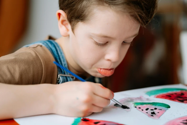 a young boy is drawing on a piece of paper, pexels contest winner, visual art, watercolour painting, dot painting, gentle expression, painting on a badge