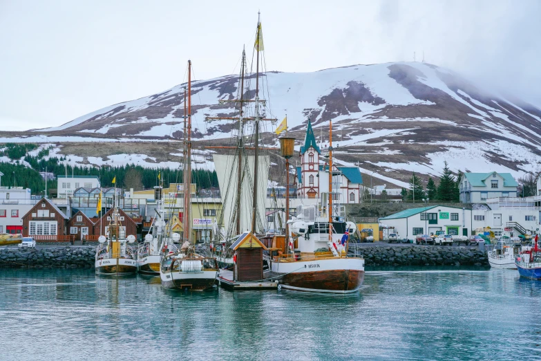 a number of boats in a body of water near a mountain, by Þórarinn B. Þorláksson, pexels contest winner, hurufiyya, wes anderson style, winter setting, square, docked at harbor