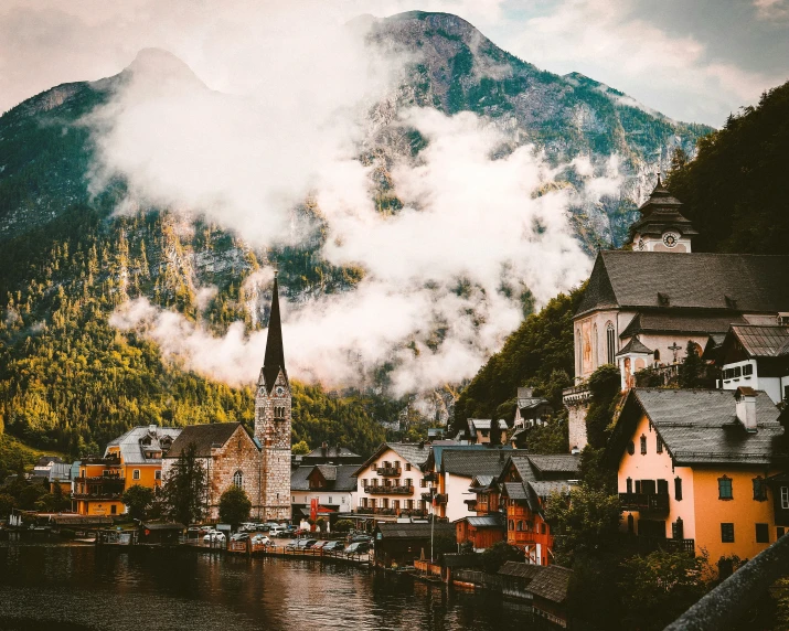 a view of a town with mountains in the background, pexels contest winner, 🦩🪐🐞👩🏻🦳, moody : : wes anderson, sound of music, building along a river