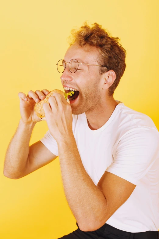 a man sitting on a stool eating a sandwich, trending on pexels, wearing yellow croptop, jewish young man with glasses, devouring, gif