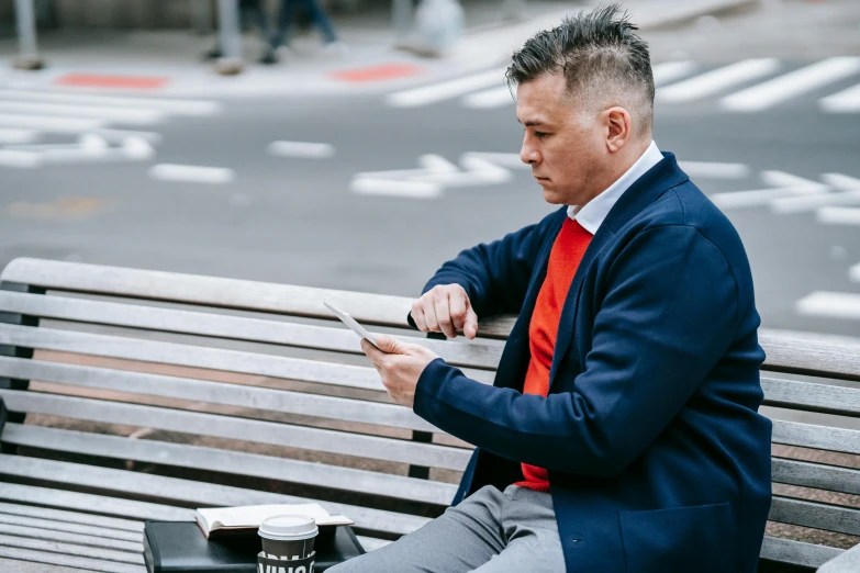 a man sitting on a bench looking at his cell phone, wearing red jacket, in chippendale sydney, wearing business casual dress, youtube thumbnail