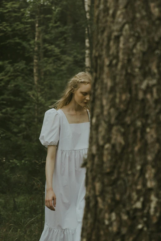a woman in a white dress standing next to a tree, by Anna Boch, unsplash contest winner, renaissance, ignant, portrait of nordic girl, film still from a horror movie, shy looking down