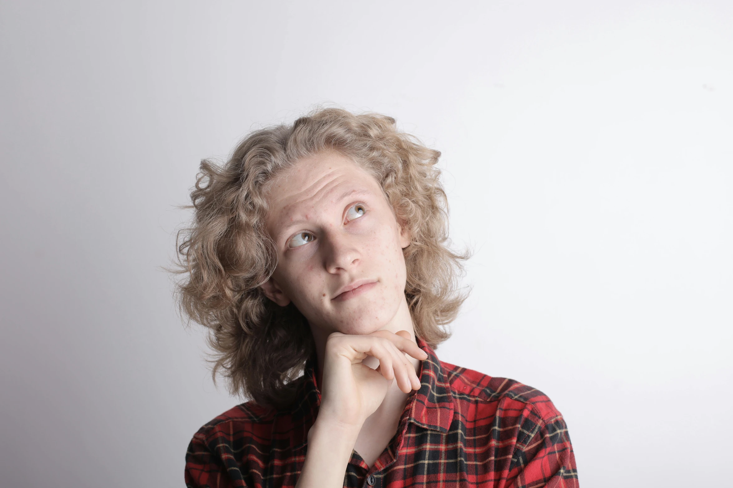 a close up of a person with a hand on their chin, pale skin curly blond hair, wearing a red lumberjack shirt, thinking pose, looking upwards